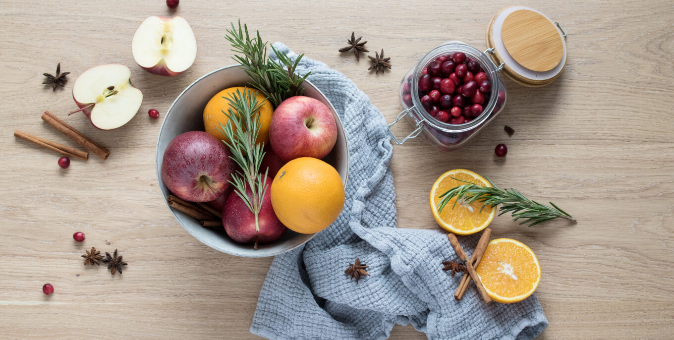 Äpfel, Orangen, Zimtstangen und Rosmarinzweige liegen auf einem Tisch.