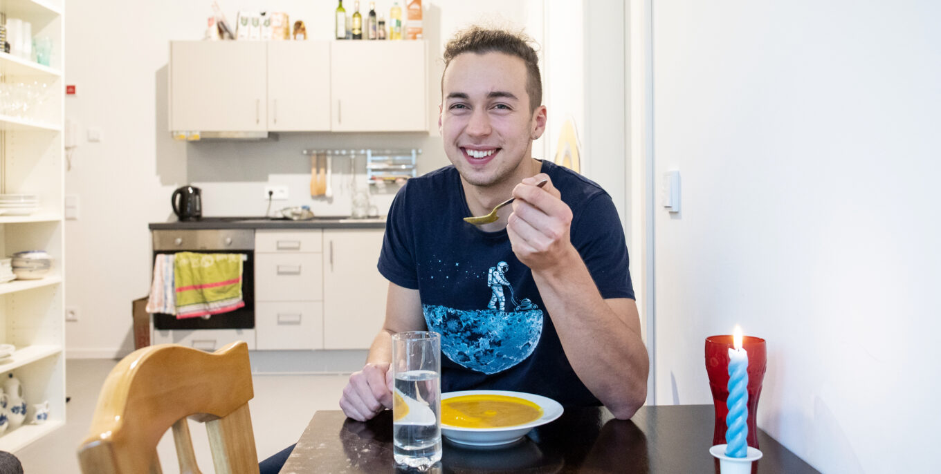 Magnus sitzt in der Küche seiner Studentenwohnung in der Bremer Straße und isst eine Suppe.