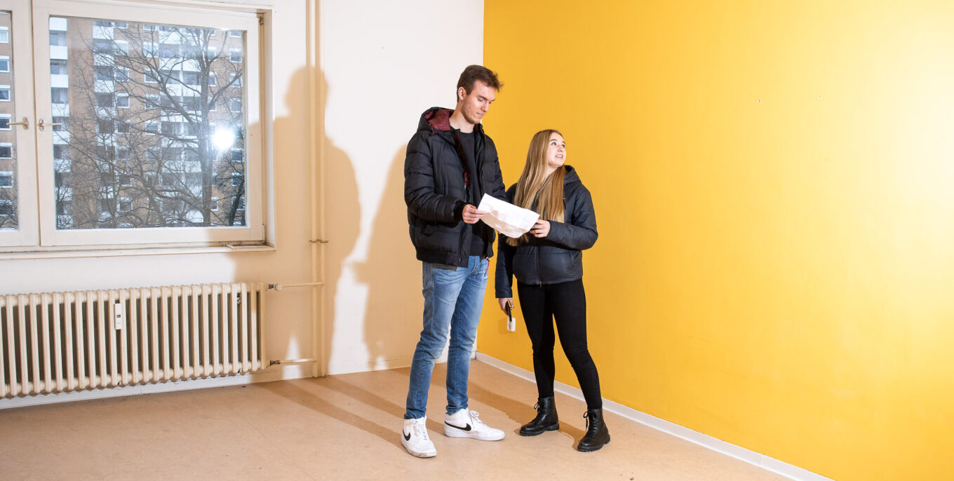 Maren und Luis machen ihre projektorientierte Ausbildung bei der Gewobag. Auf dem Foto besichtigen sie eine Wohnungen. Die Wandfarbe der Wohnung ist gelb.