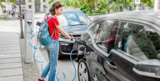 Eine Frau in rotem Shirt und hellblauer Hose lädt ein Elektroauto.