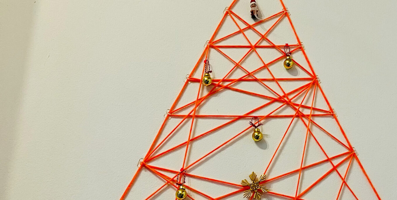 Dreieck aus orangeroten Fäden mit kleinen goldfarbenen Weihnachtskugeln.