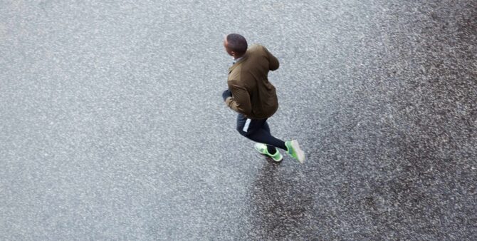 Vogelperspektive eines Mannes, der nach dem Regen auf einer glänzenden Straße läuft, mitten im Geschehen