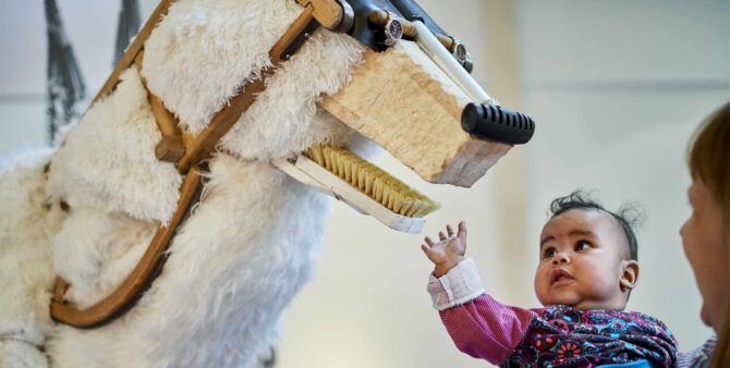 Ein Baby berührt eine Tierskulptur in der Ausstellung Anoha – Die Kinderwelt des Jüdischen Museums Berlin