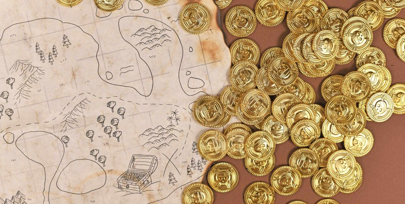 Eine Piratenschatzkarte liegt auf einem Tisch. Daneben goldfarbene Münzen mit Piratenschädel darauf.