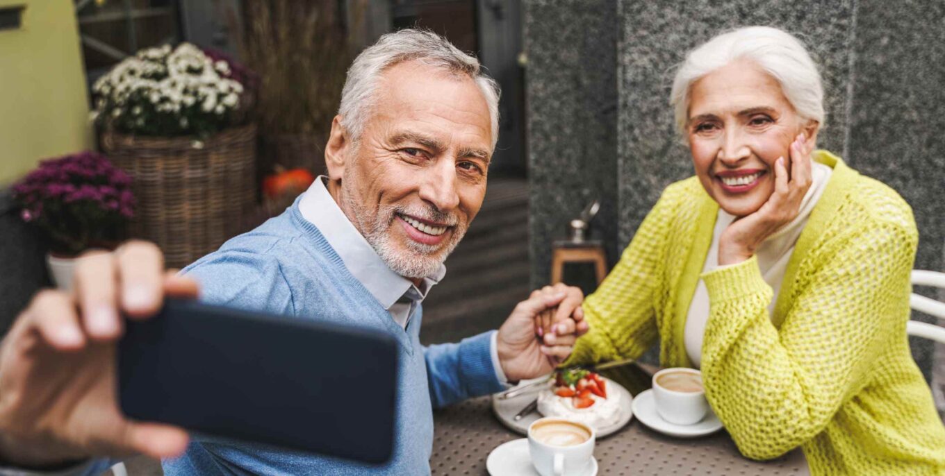 Älteres Paar in einem Café, das Händchen hält und ein Selfie von sich macht