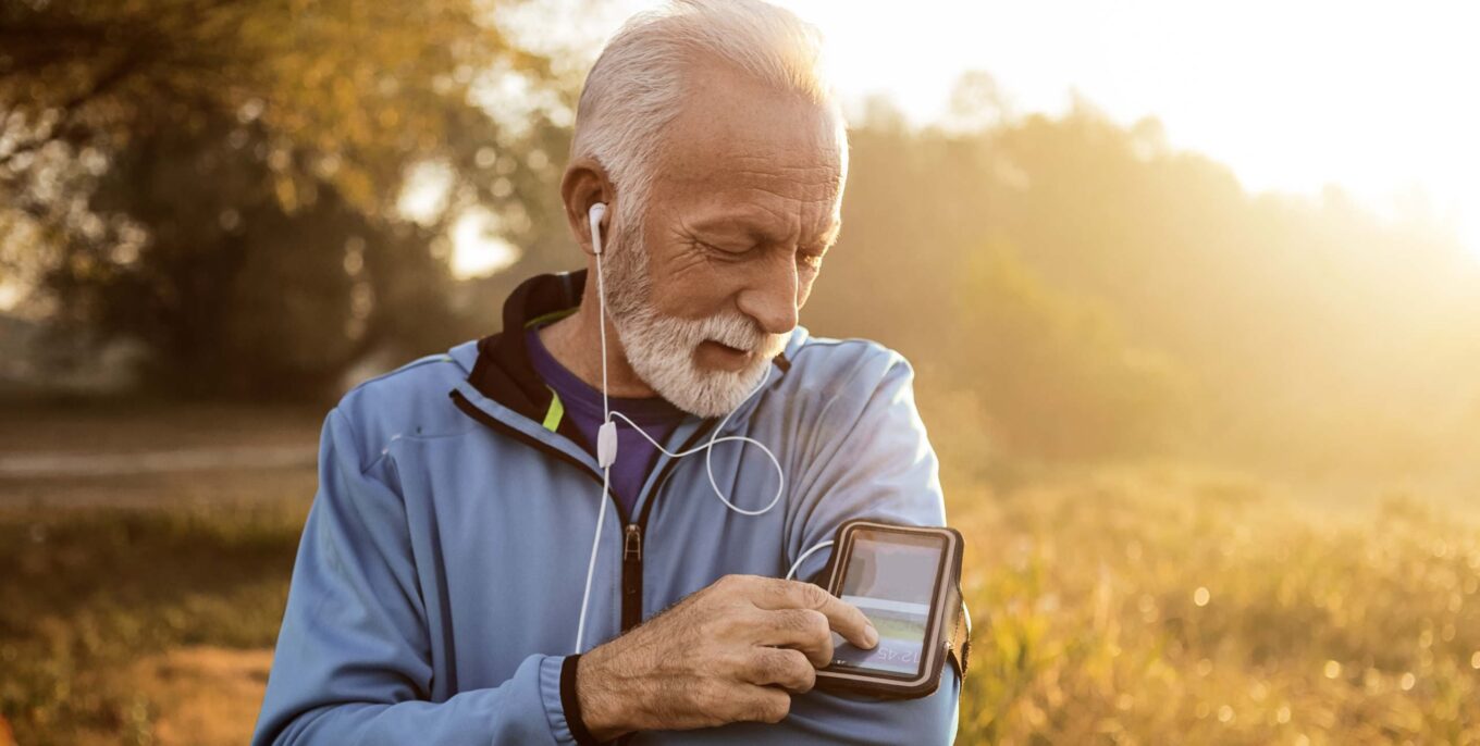 Ältere Läufer in der Natur mit Smartphone und Kopfhörern.