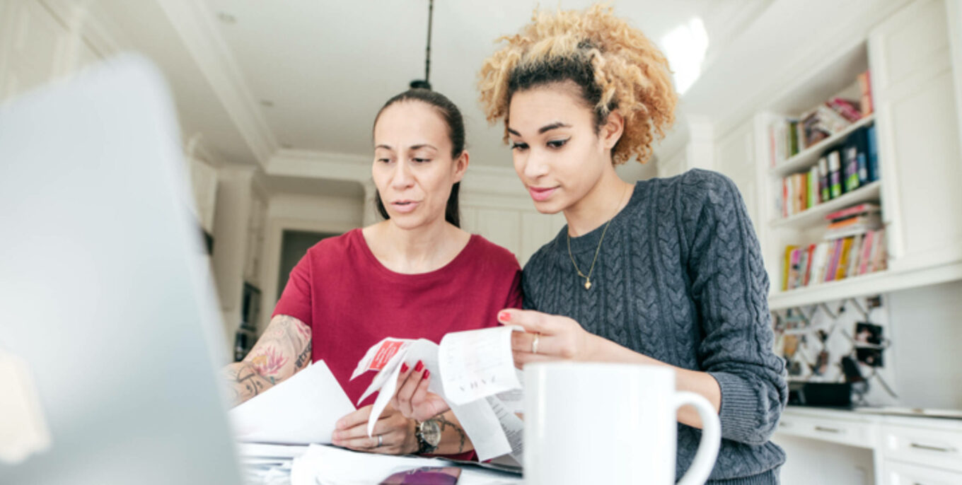 Eine Frau unterstützt eine jüngere Frau bei der Steuererklärung. Gemeinsam schauen sie auf Rechnungen.