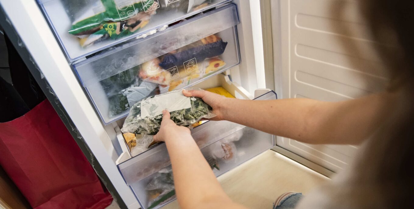 Frau nimmt eine Tüte mit gefrorenem Mischgemüse aus dem Kühlschrank.