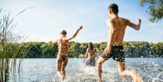 Eine Gruppe von Menschen in Badekleidung, die an einem sonnigen Nachmittag in einen See laufen.