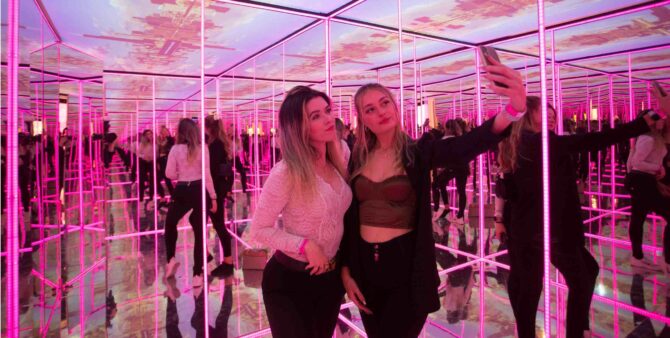 Zwei junge Frauen nehmen in einem Spiegelraum ein Selfie auf