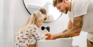 Junger weißer Vater hilft seiner kleinen Tochter beim Händewaschen im Badezimmer.