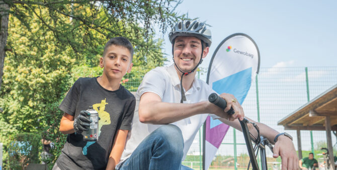 Ein Mitarbeiter der BEGSpo posiert auf einem BMX-Rad. Neben ihm posiert ein Junge, der eine Spraydose in der Hand hält. Foto: Felix Seyfert