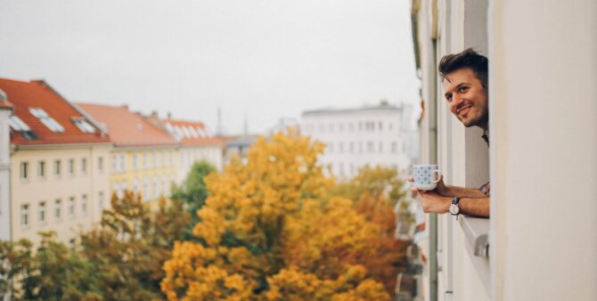 Ein junger Mann trinkt Kaffee und blickt aus dem Fenster einer Wohnung in Berlin, Prenzlauer Berg.