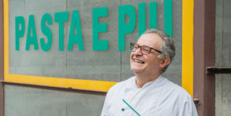 Reza Mohammadi steht vor seiner Pastamanufaktur Pasta e Più und lächelt in die Kamera. Er trägt einen weißen Kittel und eine Brille. Foto: Felix Seyfert