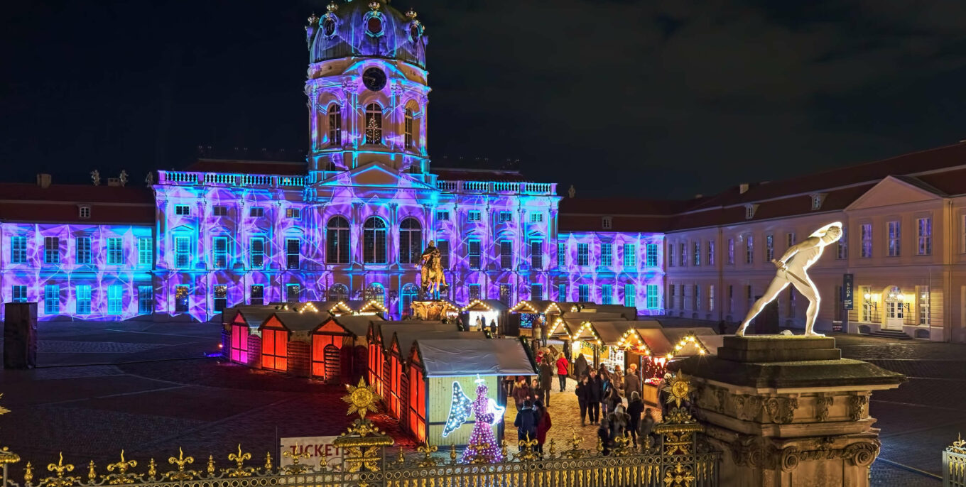 Weihnachtsmärkte in Berlin: Blick auf eine kleine Reihe beleuchteter Stände vor dem illuminierten Schloss Charlottenburg.