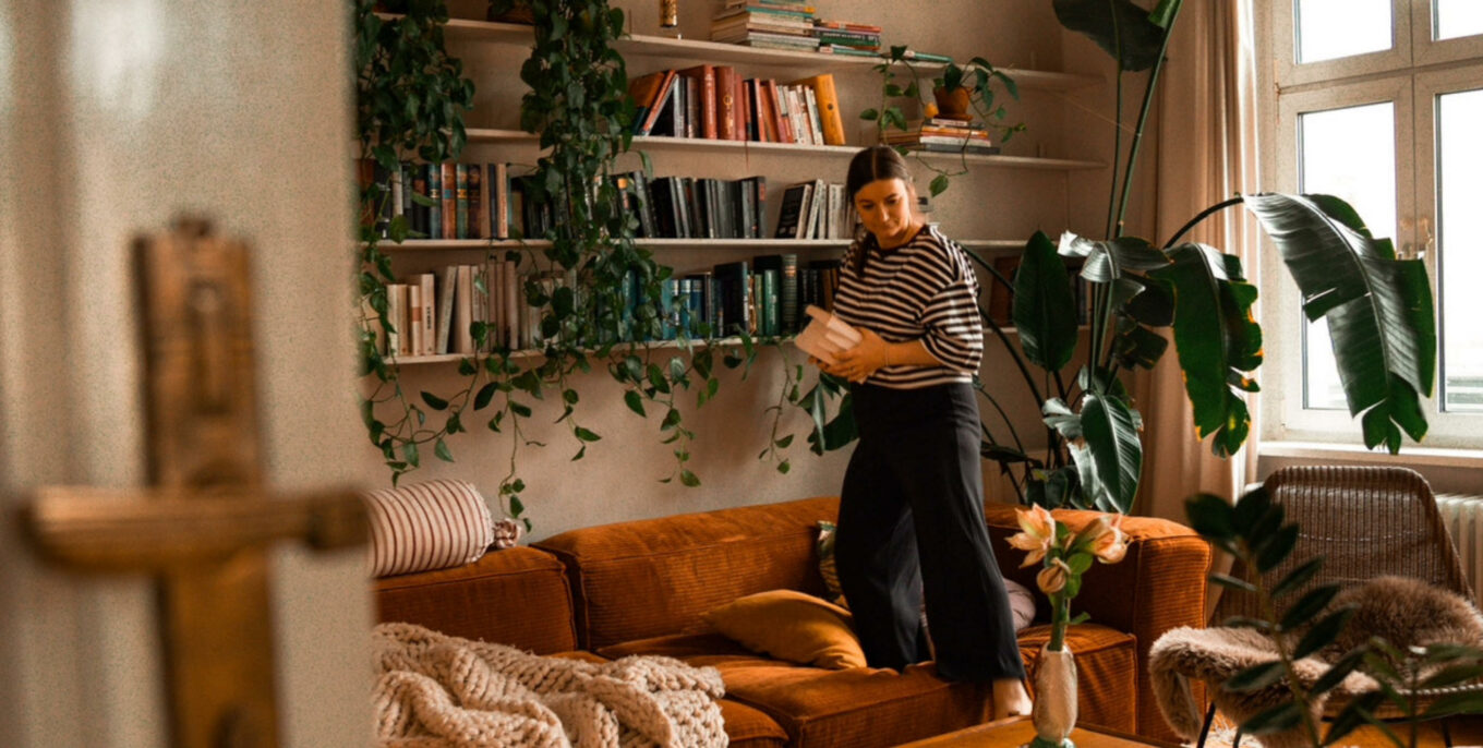 Kleine Wohnzimmer: Blick durch die Tür in ein Wohnzimmer, eine Frau steigt gerade vom Sofa herab, sie hat Bücher von einem Regalbrett über dem Sofa genommen. Foto: Mimi Vollgraf