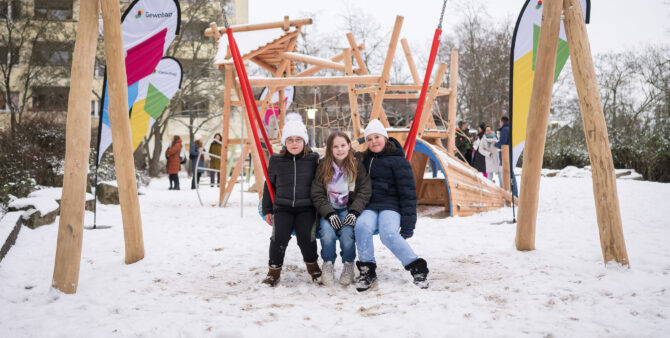 Drei junge Mädchen sitzen auf einer neuen Netzschaukel auf einem verschneiten Spielplatz. Foto: Moritz Eden/City-Press GmbH