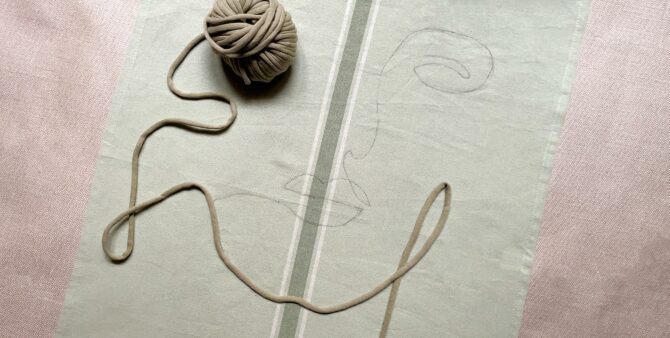 Ein Faden wird auf eine vorgezeichnete Linie auf einem Stück Stoff gelegt.