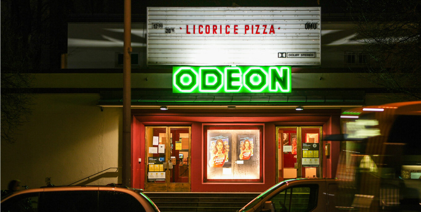 Das Odeon von außen: eine Anzeigetafel, ein grünes Neon-Logo und Filmplakate. 