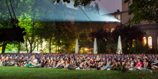 Großes Freiluftkino bei Nacht im Park mit zahlreichen Zuschauern auf Liegestühlen und Decken