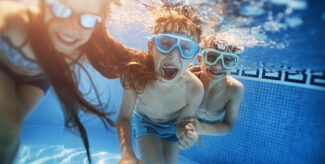 Kinder tauchen mit Schwimmbrillen im blauen Wasser eines Schwimmbeckens und haben Spaß