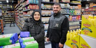 Eine Frau mit Kopftuch und ein Mann stehen in einem Supermarkt und lächeln in die Kamera. Foto: Andreas Labes