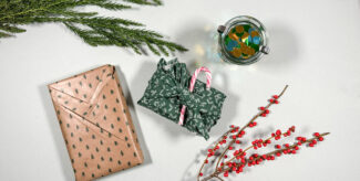 Drei verschiedenartig verpackte Weihnachtsgeschenke auf hellem Untergrund, flankiert von natürlichen Zweigen. Foto: Laetitia Delorme