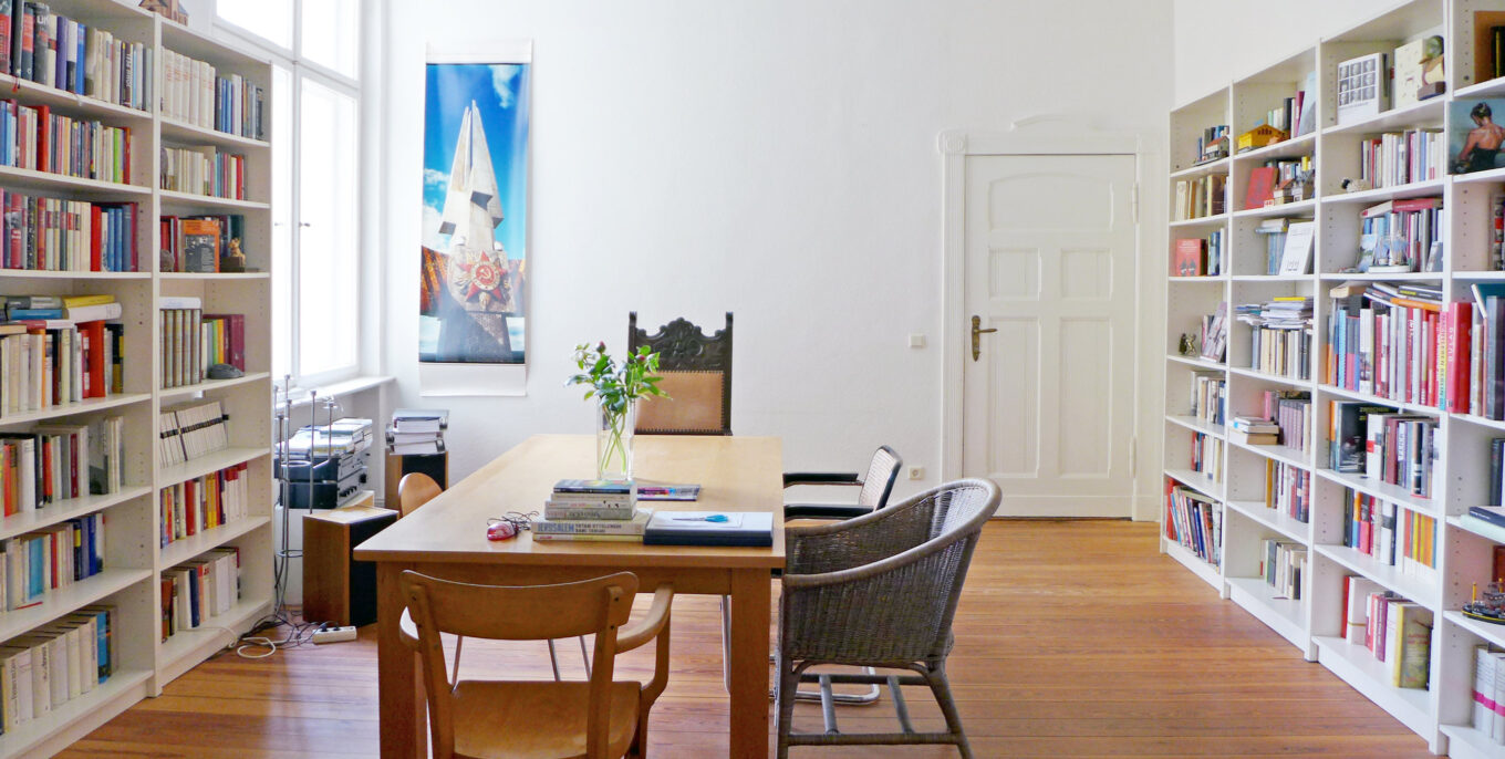 Berliner Zimmer mit Bücherregalen an den Wänden und einem großen Esstisch mit Stühlen in der Mitte. 