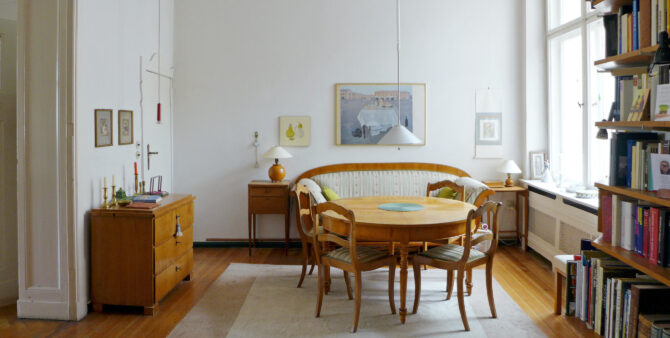 Elegantes Esszimmer mit rundem Holztisch, gepolsterter Sitzbank und antiken Möbeln, ergänzt durch Bücherregale und Wanddekoration.
