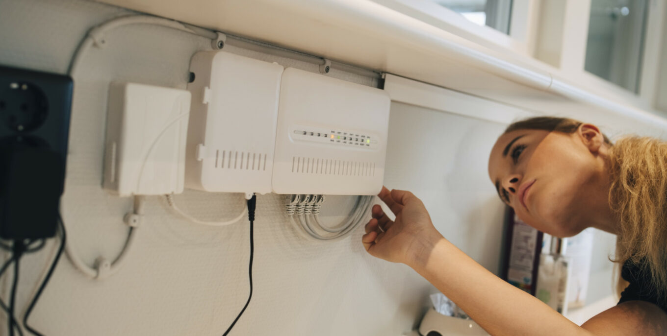 Frau überprüft weißen Router an Wand mit mehreren angeschlossenen Netzwerkkabeln