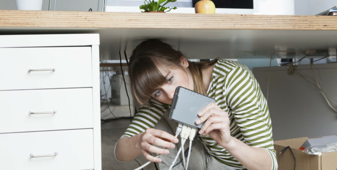 Frau unter Schreibtisch schließt Netzwerkkabel an schwarzen Router an