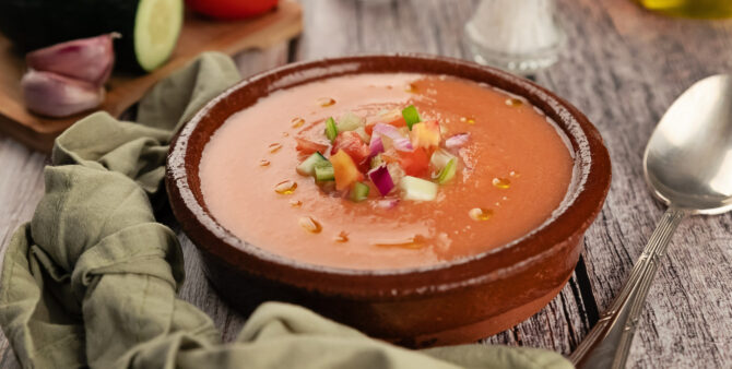 Kalte Tomatensuppe in Tonschale, garniert mit frischen Gemüsewürfeln und Olivenöl.