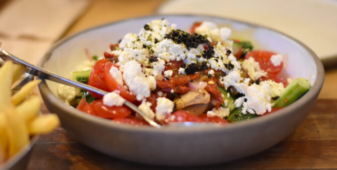 Griechischer Salat mit Tomaten, Gurken, Paprika und Feta in grauer Schüssel serviert.