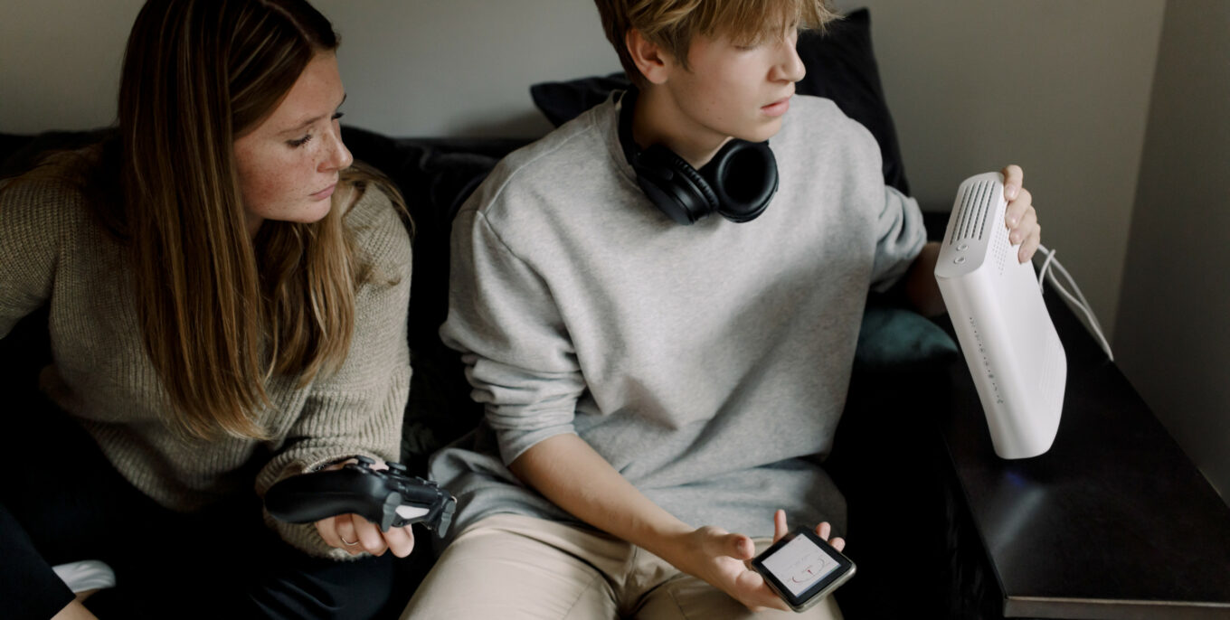 Zwei junge Erwachsene prüfen WLAN-Router, eine hält Smartphone, die andere einen Spielecontroller