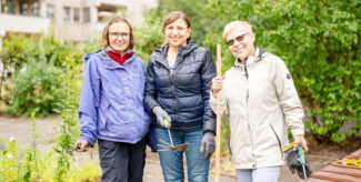 Drei Menschen stehen im Garten und halten Gartenwerkzeuge, umgeben von grünen Pflanzen. Foto: Ralph Maak