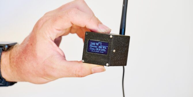 Großaufnahme: Ein Hand hält ein kleines rechteckiges Kontrolltool mit Antenne und Display, das die Leistung eines Steckersolargeräts erfasst. Foto: Andreas Labes