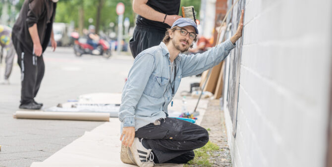 Ein Mann mit Brille und Basecap kniet vor einer Wand, um ein Foto anzubringen. Foto: Felix Seyfert