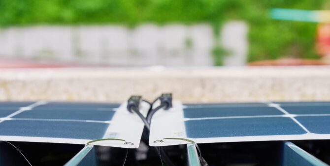 Steckersolargerät, Ansicht von oben: Zwei dünne Photovoltaik-Module, die mit metallischen Kabelbindern an einem Balkongeländer befestigt sind. Foto: Andreas Labes