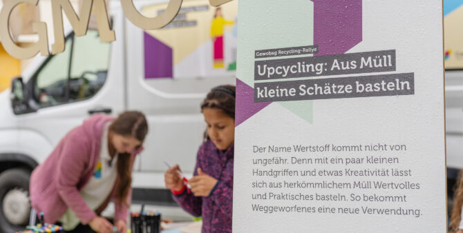 Eine Person bastelt an einem Tisch vor einem Schild mit der Aufschrift "Upcycling: Aus Müll kleine Schätze basteln". Foto: Felix Seyfert