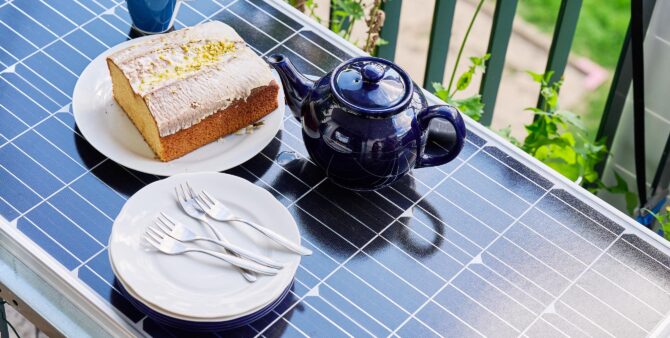 Großaufnahme: Eine Teekanne, ein Kuchen und Kuchenteller auf einem Balkontisch, der aus einem Photovoltaik-Modul besteht. Foto: Andreas Labes