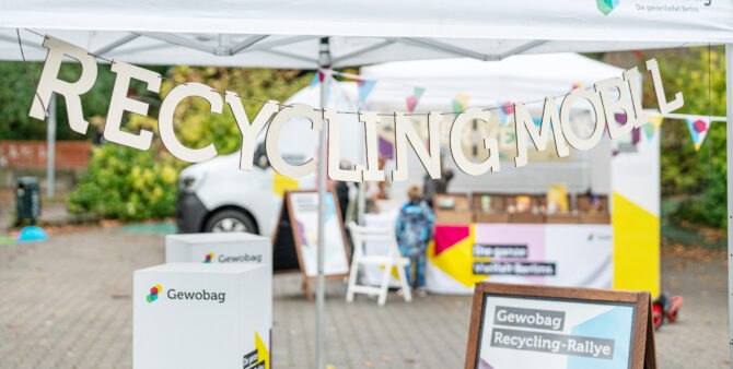 Eine Holzgirlande mit der Aufschrift "Recycling Mobil", im Hintergrund ein Eventstand der Gewobag Recycling-Rallye. Foto: Felix Seyfert