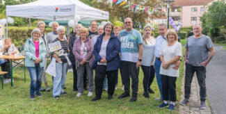 Eine Gruppe von Personen steht bei einem Outdoor-Event unter einem Pavillon neben einem Tisch mit Dekorationen, darunter Luftballons und bunte Wimpel. Foto: Felix Seyfert