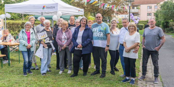 Eine Gruppe von Personen steht bei einem Outdoor-Event unter einem Pavillon neben einem Tisch mit Dekorationen, darunter Luftballons und bunte Wimpel. Foto: Felix Seyfert