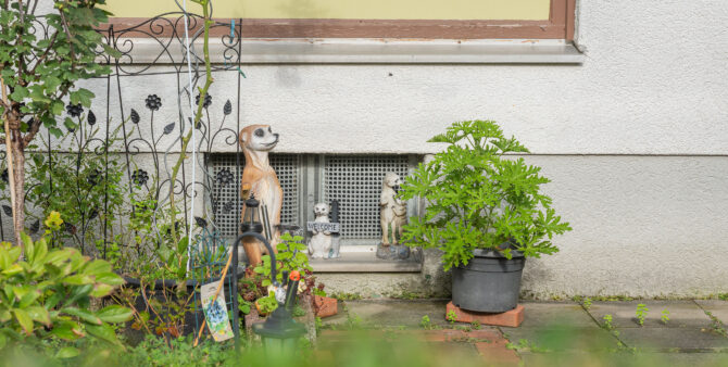 Die Gartenansicht zeigt Tierstatuen und Pflanzen vor einem Kellerfenster mit einem dekorativen Spalier. Foto: Felix Seyfert