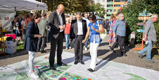 Zwei Frauen und zwei Männer stehen auf einem großen Transparent, auf dem markierte Punkte in einem Stadtquartier zu sehen sind. Eine der Frauen erklärt etwas. Foto: Jennifer Sanchez