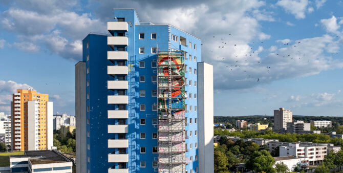 Ein teilweises eingerüstetes Hochhaus, an dem ein großes Wandbild entsteht. Foto: Jennifer Sanchez