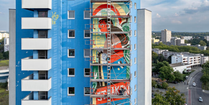 Ein teilweises eingerüstetes Hochhaus, an dem ein großes Wandbild entsteht. Foto: Jennifer Sanchez