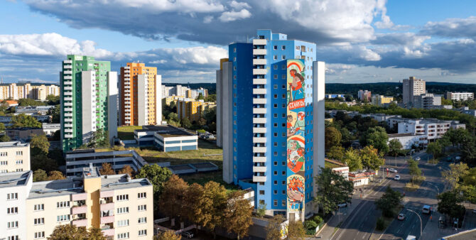 Drohnenaufnahme: Ein blau-weißes Hochhaus, an dem ein buntes, 50 Meter hohes Wandbild prangt. Foto: Jennifer Sanchez