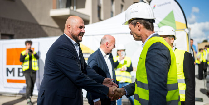 Zwei Männer auf einer Baustelle schütteln sich zur Begrüßung die Hände und lächeln. Foto: City-Press GmbH
