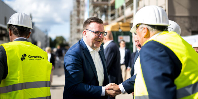 Zwei Männer auf einer Baustelle schütteln sich zur Begrüßung die Hände und lächeln. Foto: City-Press GmbH